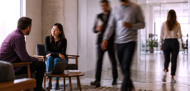 Pessoas conversando em uma área de escritório com outras pessoas caminhando ao fundo.