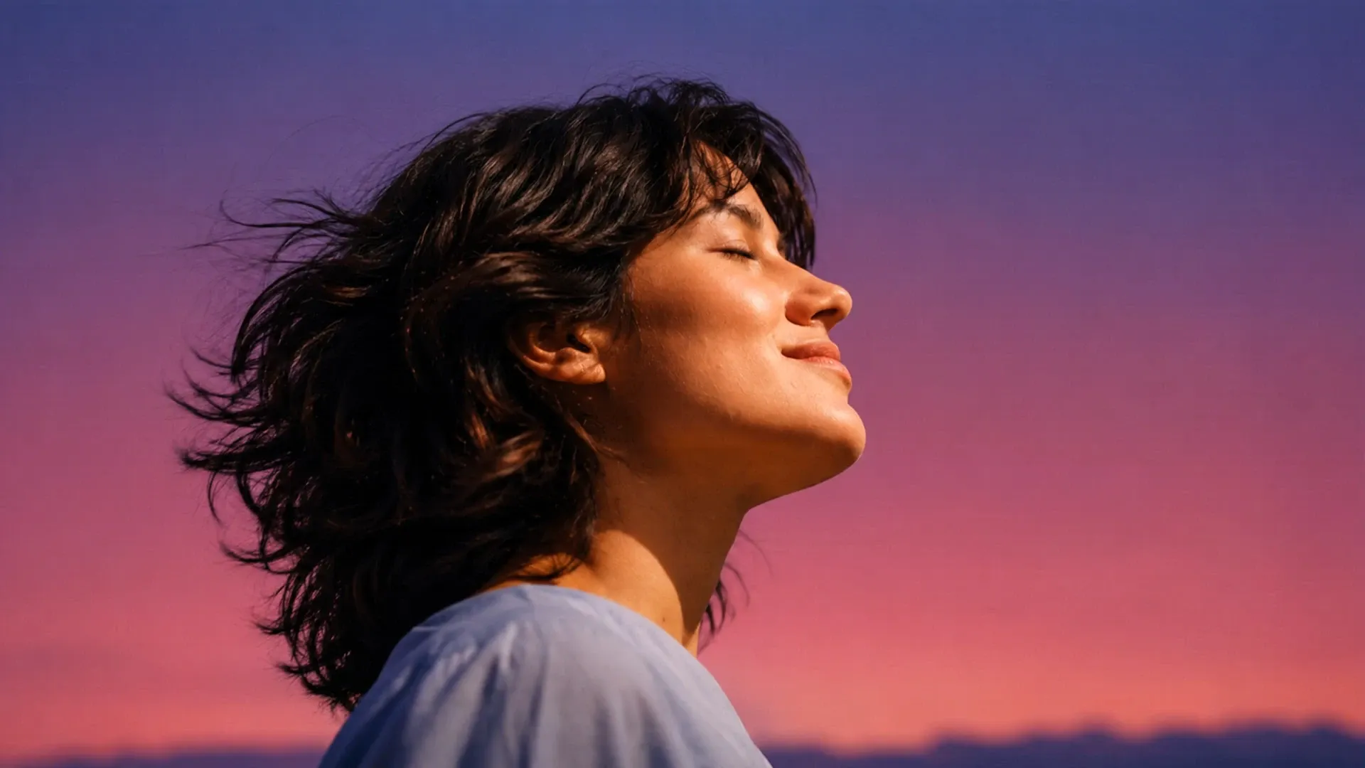 Mulher de perfil com os olhos fechados diante de um céu ao entardecer.